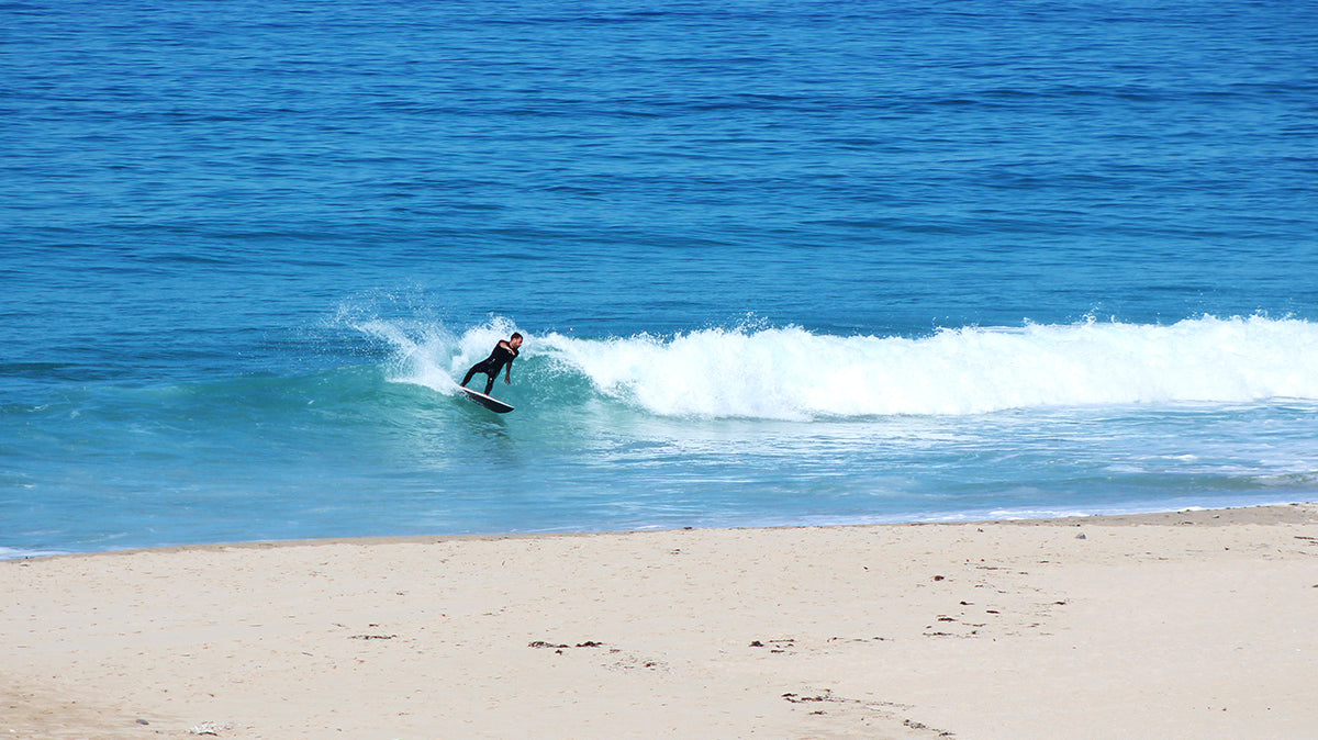 surfer in a bright blue sea does a turn in front of empty sandy beach