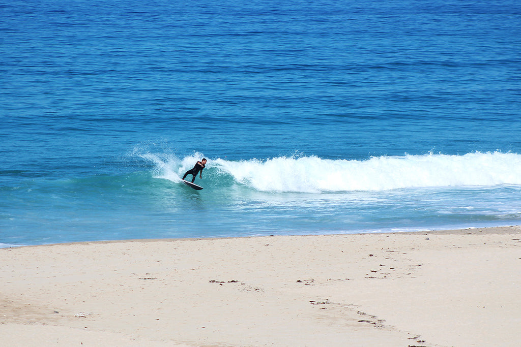 surfer in a bright blue sea does a turn in front of empty sandy beach